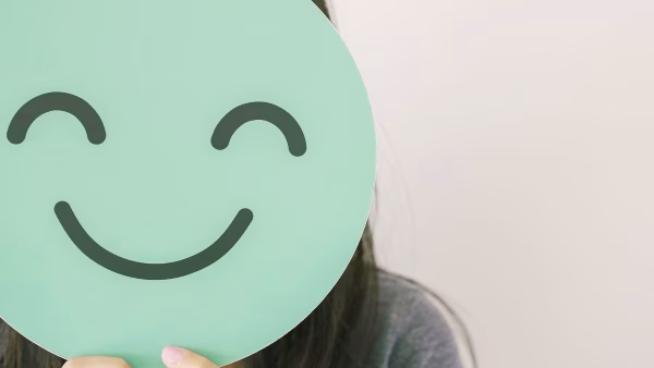 meisje wat zich verstopt achter een groen masker met blije smiley